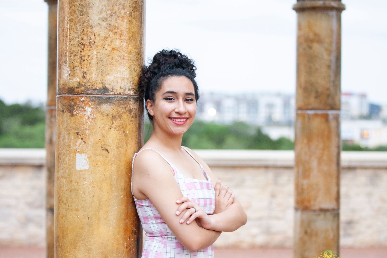 A portrait taken against yellow architectural columns with cityscape in background.