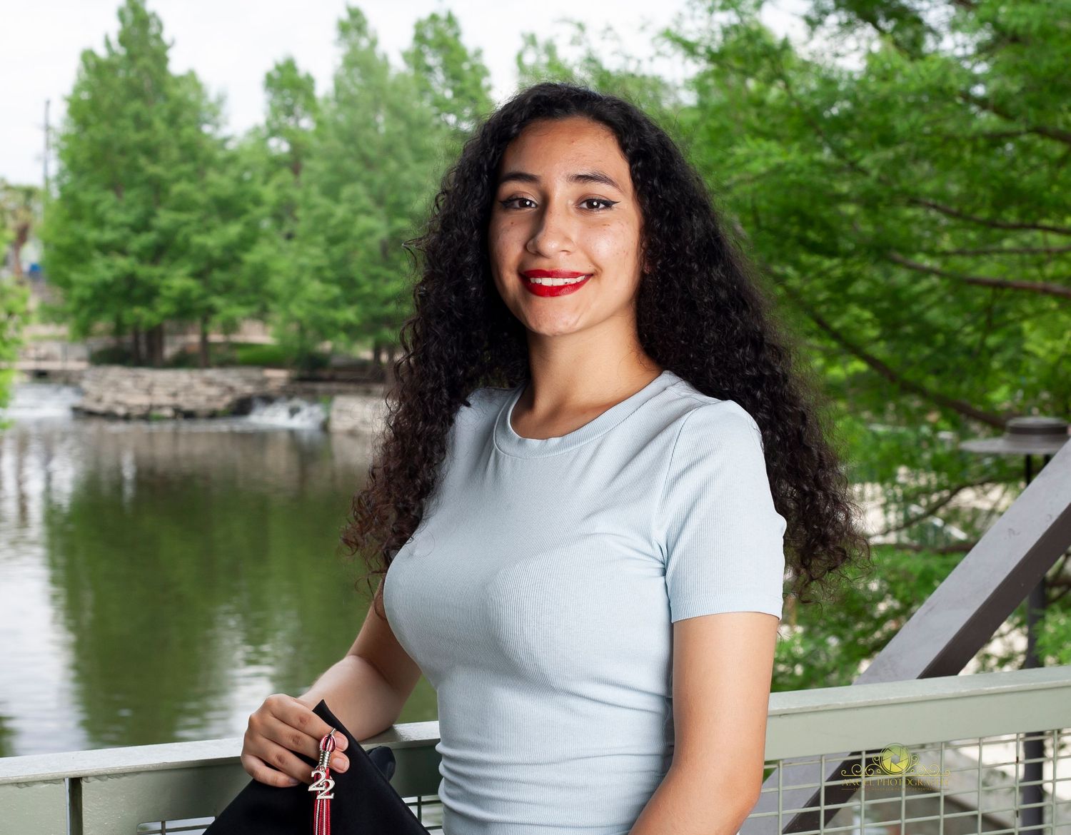 A portrait taken on a bridge overlooking a scenic pond with lush green trees in the background.