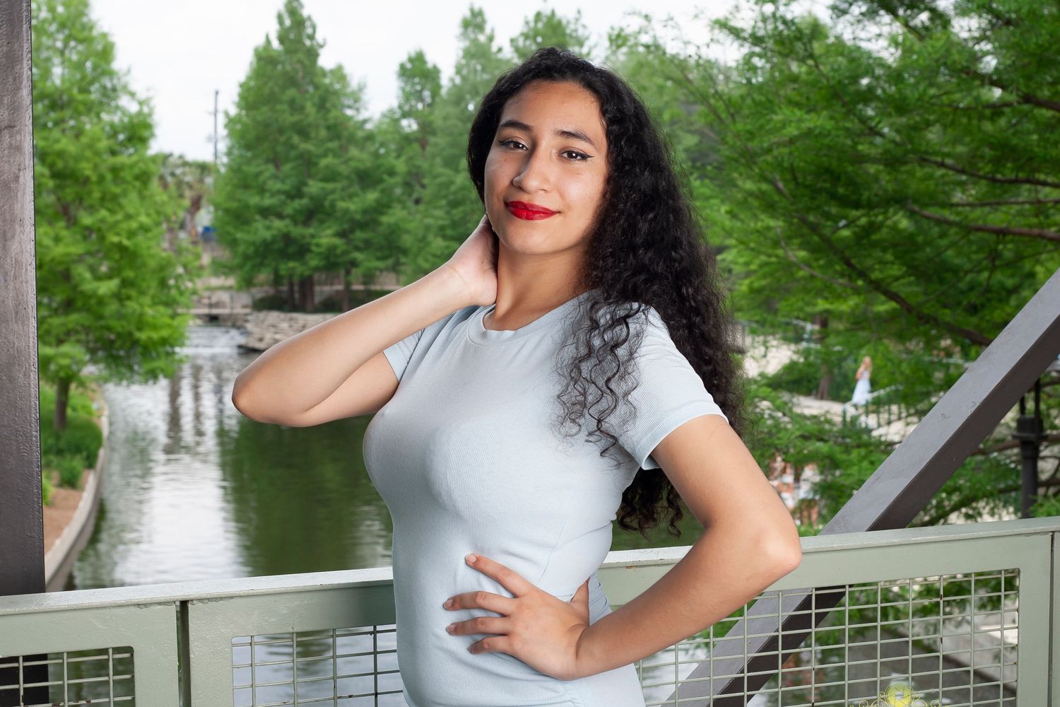Casual outdoor portrait with water and greenery in the background on a sunny day.