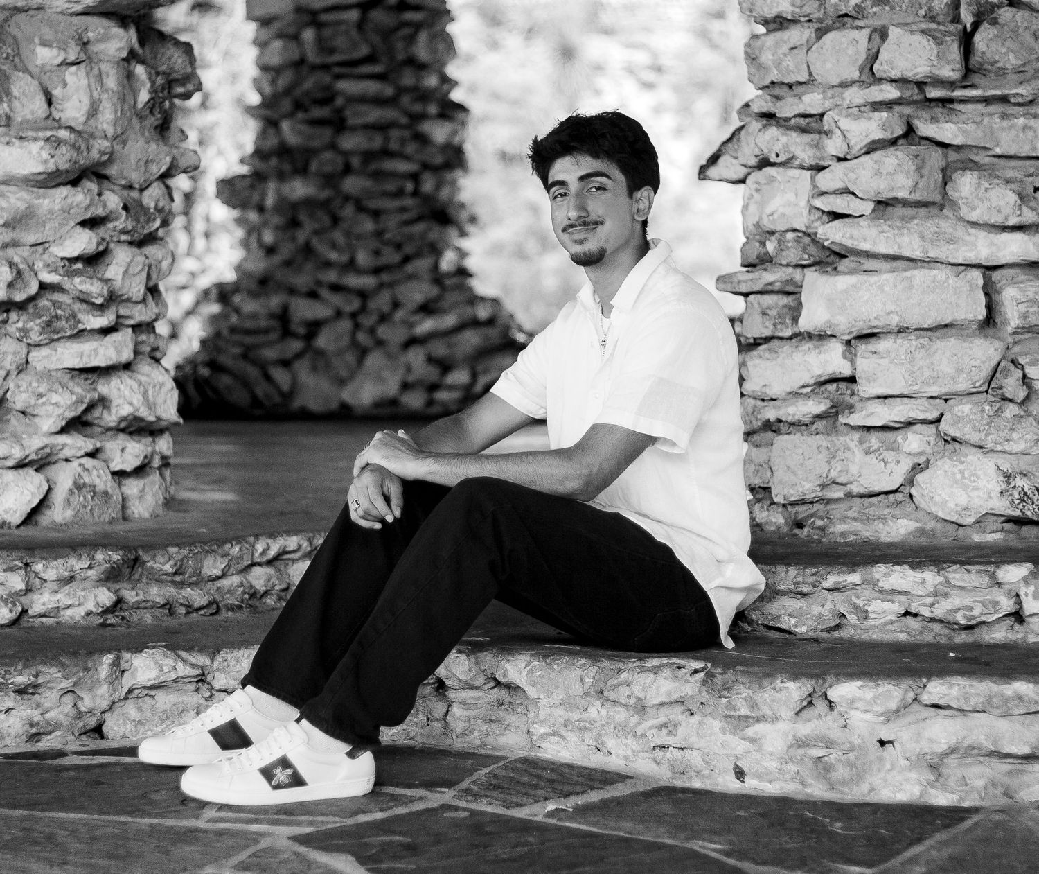 Black and white photo of someone sitting on stone ledge wearing casual attire.
