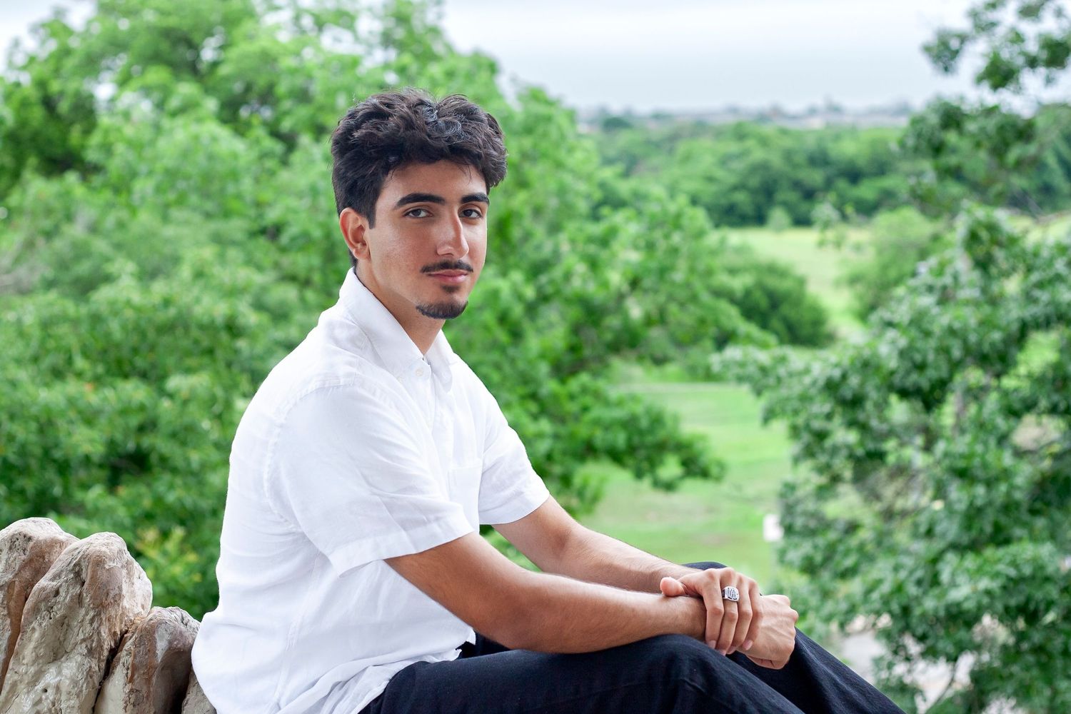 Someone in white shirt sits on stone wall with green landscape in background.