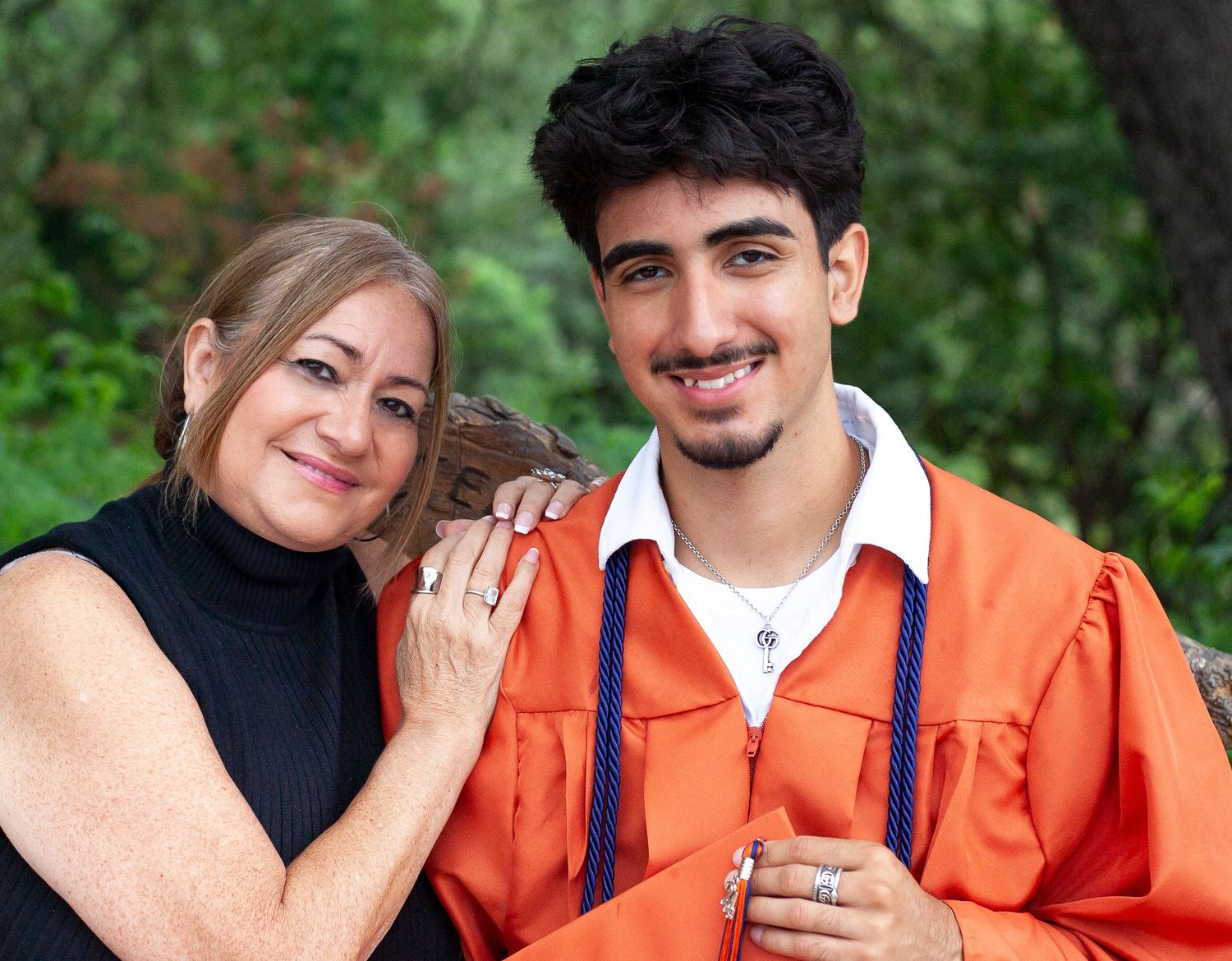 A graduation photo with orange academic regalia against natural backdrop.