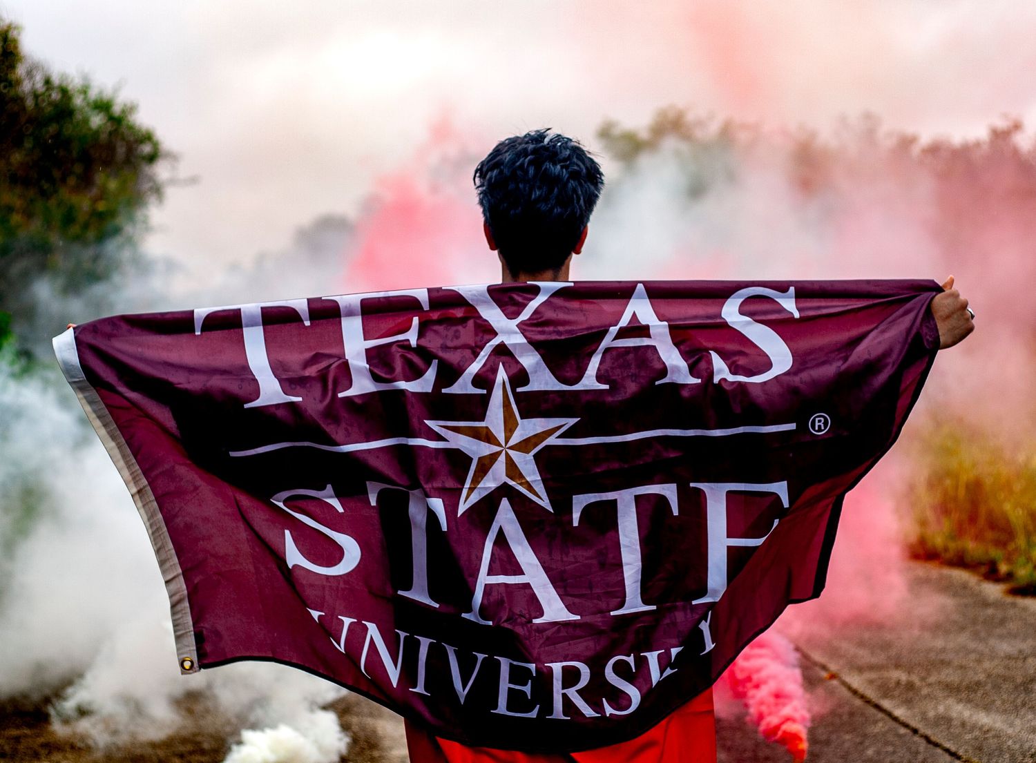 Texas State University banner displayed with colorful smoke effects in the background.