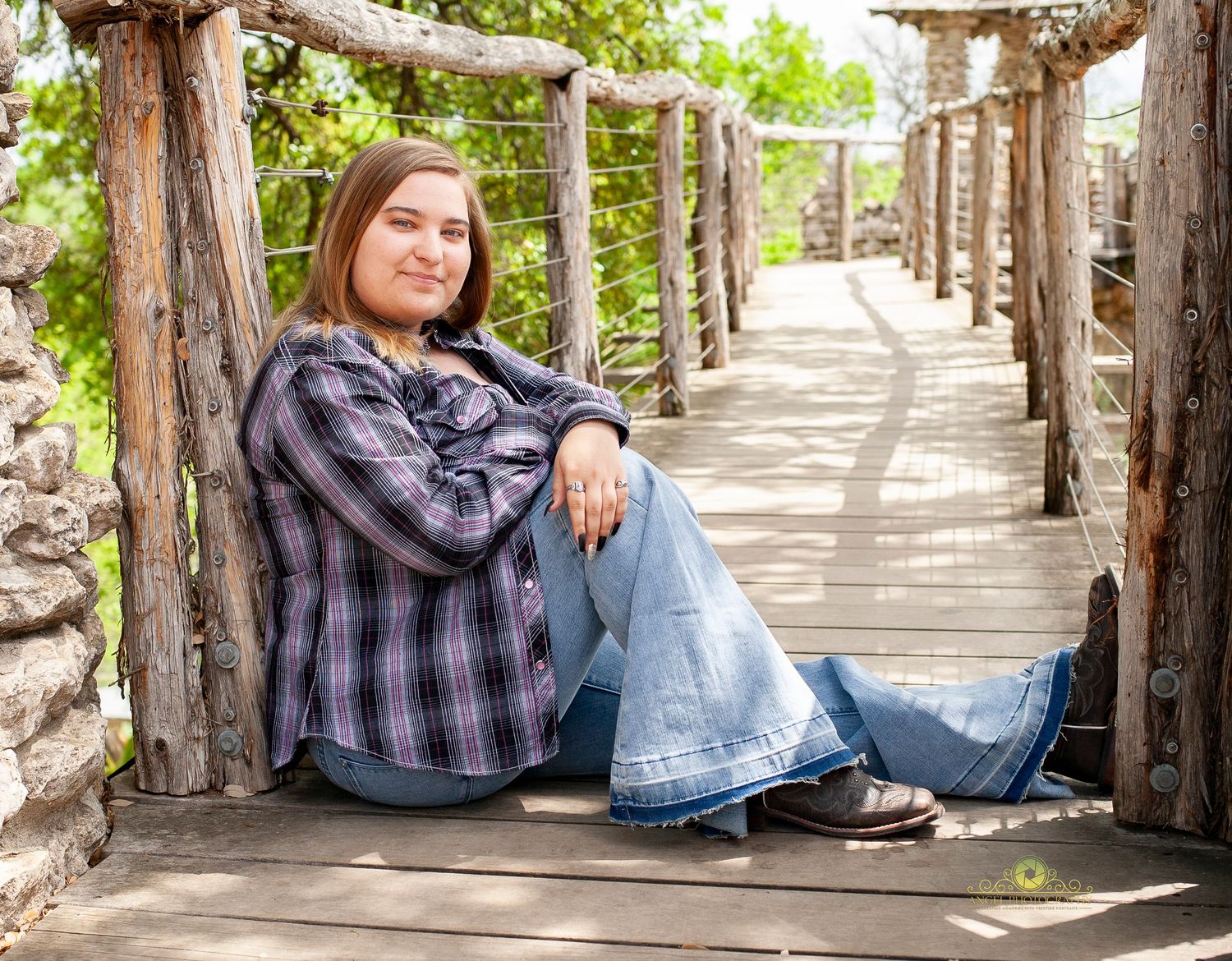 Senior portrait on rustic wooden bridge wearing plaid shirt and jeans.