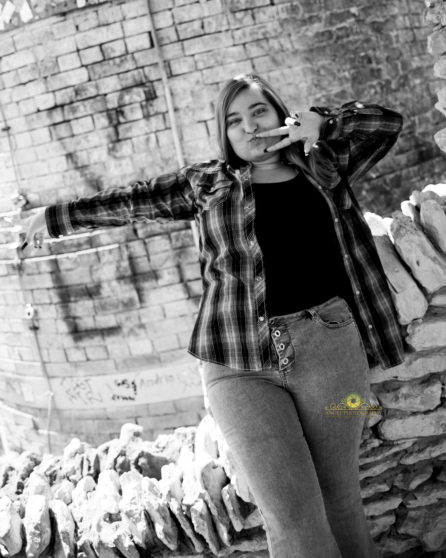 Black and white portrait of someone in plaid shirt posing against graffiti wall.