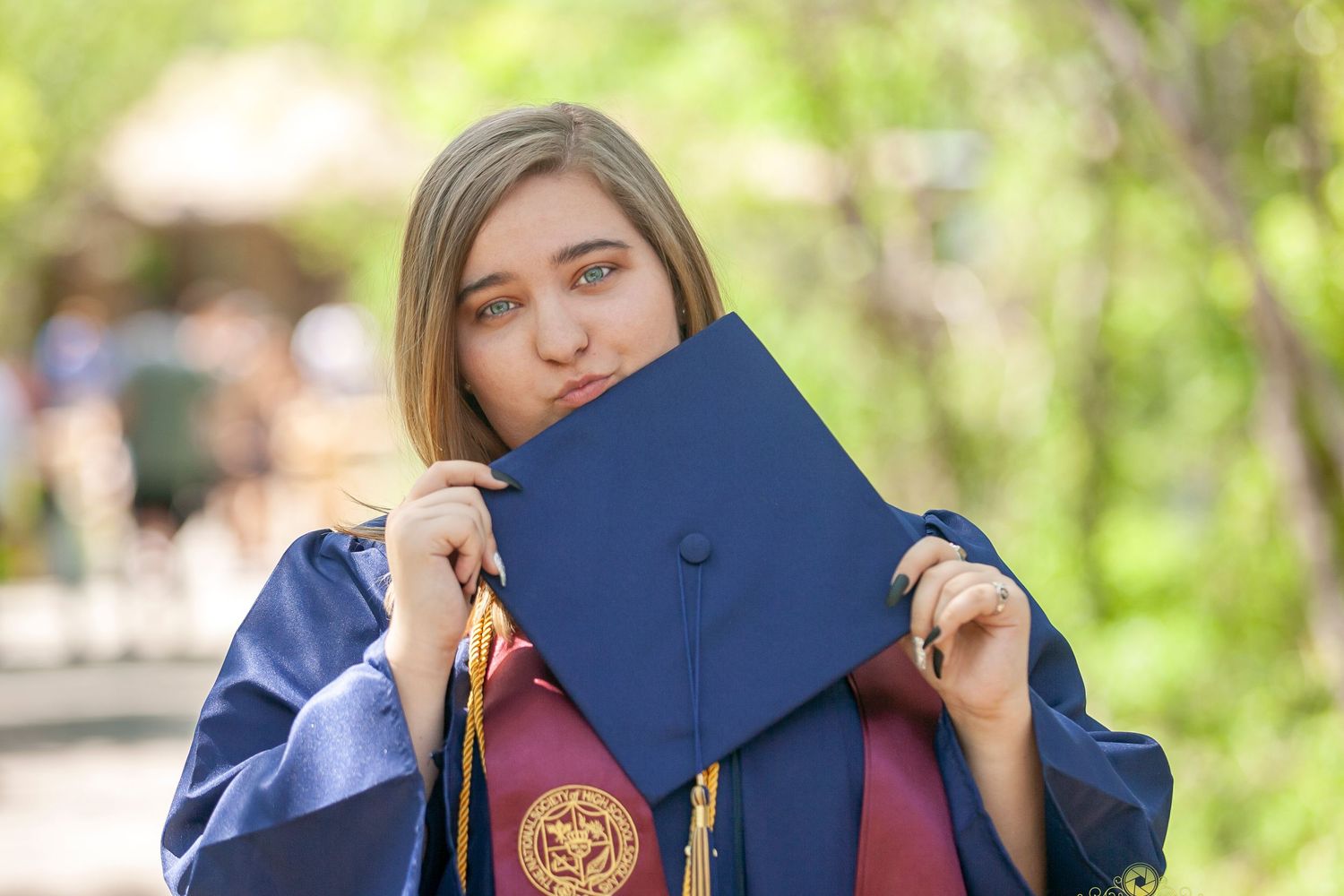 Graduate holds up blue mortarboard while wearing traditional commencement regalia.
