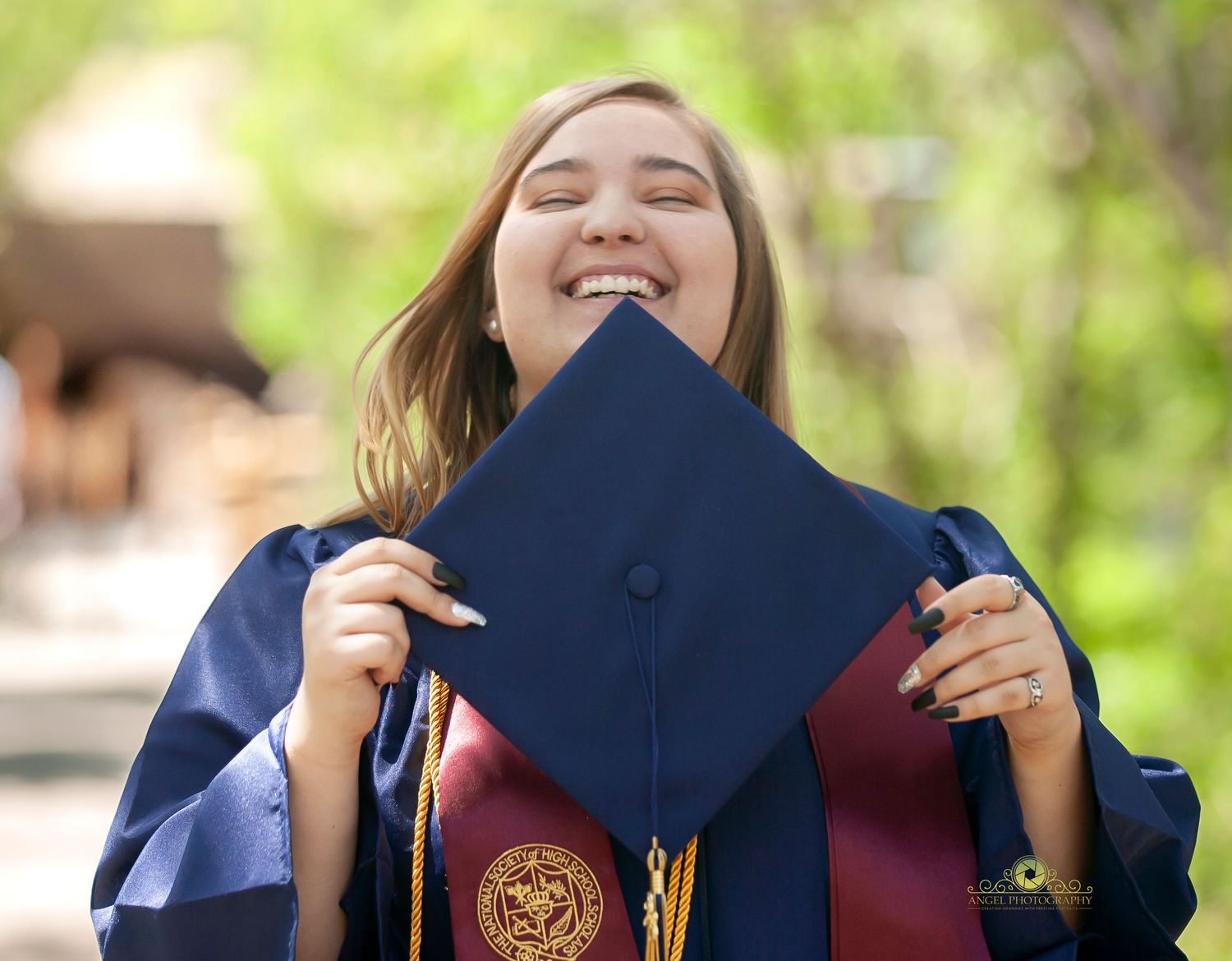 Graduate in blue gown shows joyful expression while holding mortarboard.