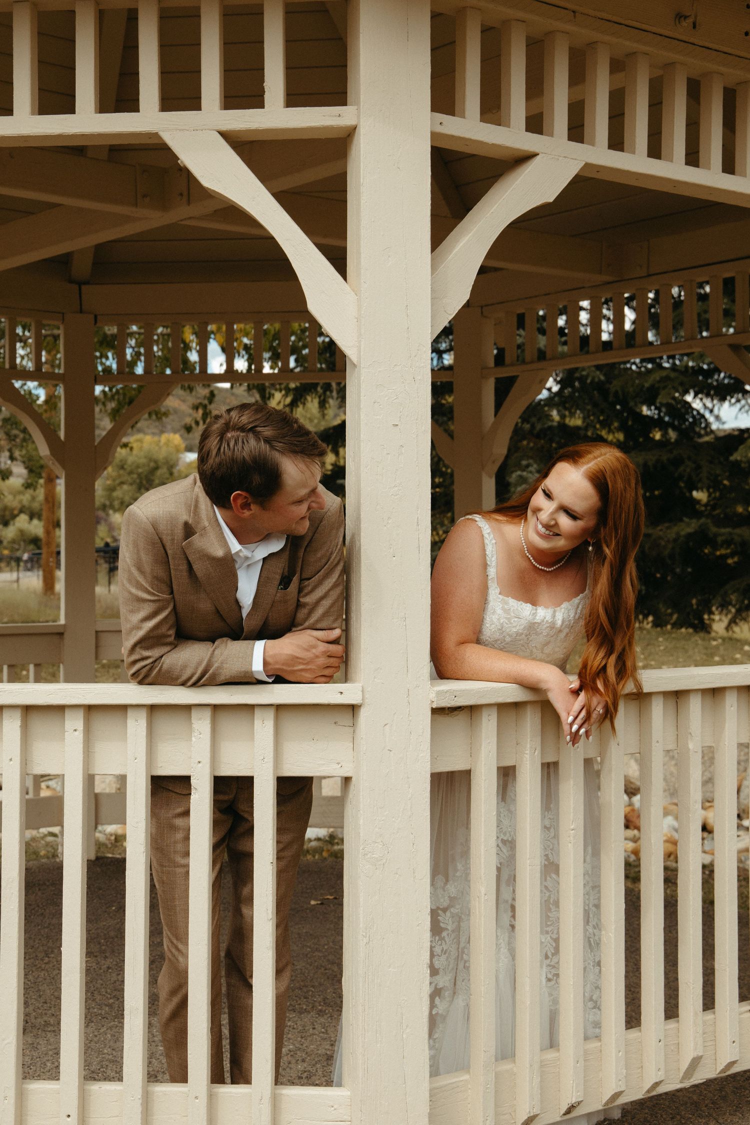 Playful couple leaning on white gazebo railing in romantic wedding photo sequence.