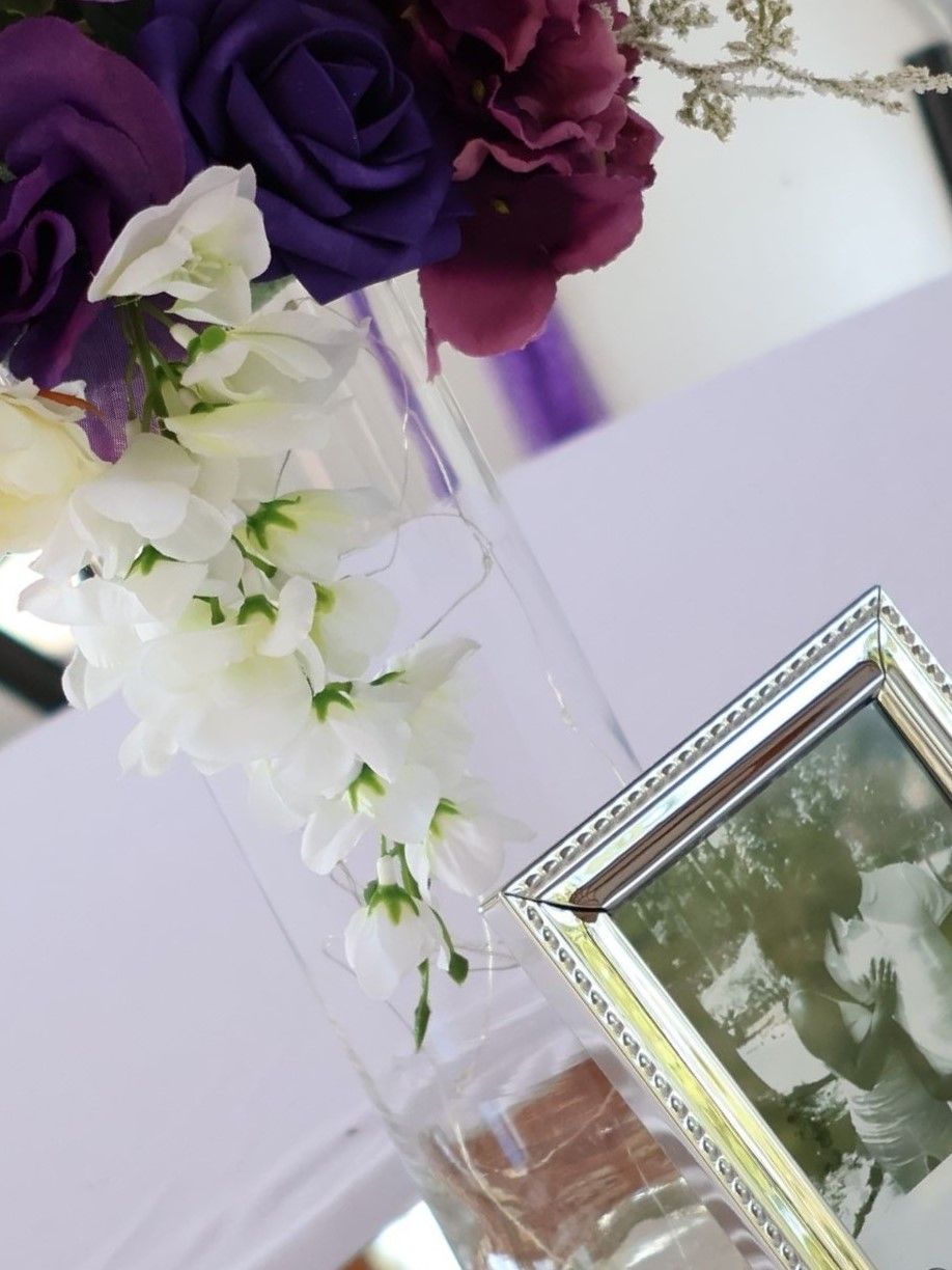 Purple and white floral arrangements with picture frames on display at an event.