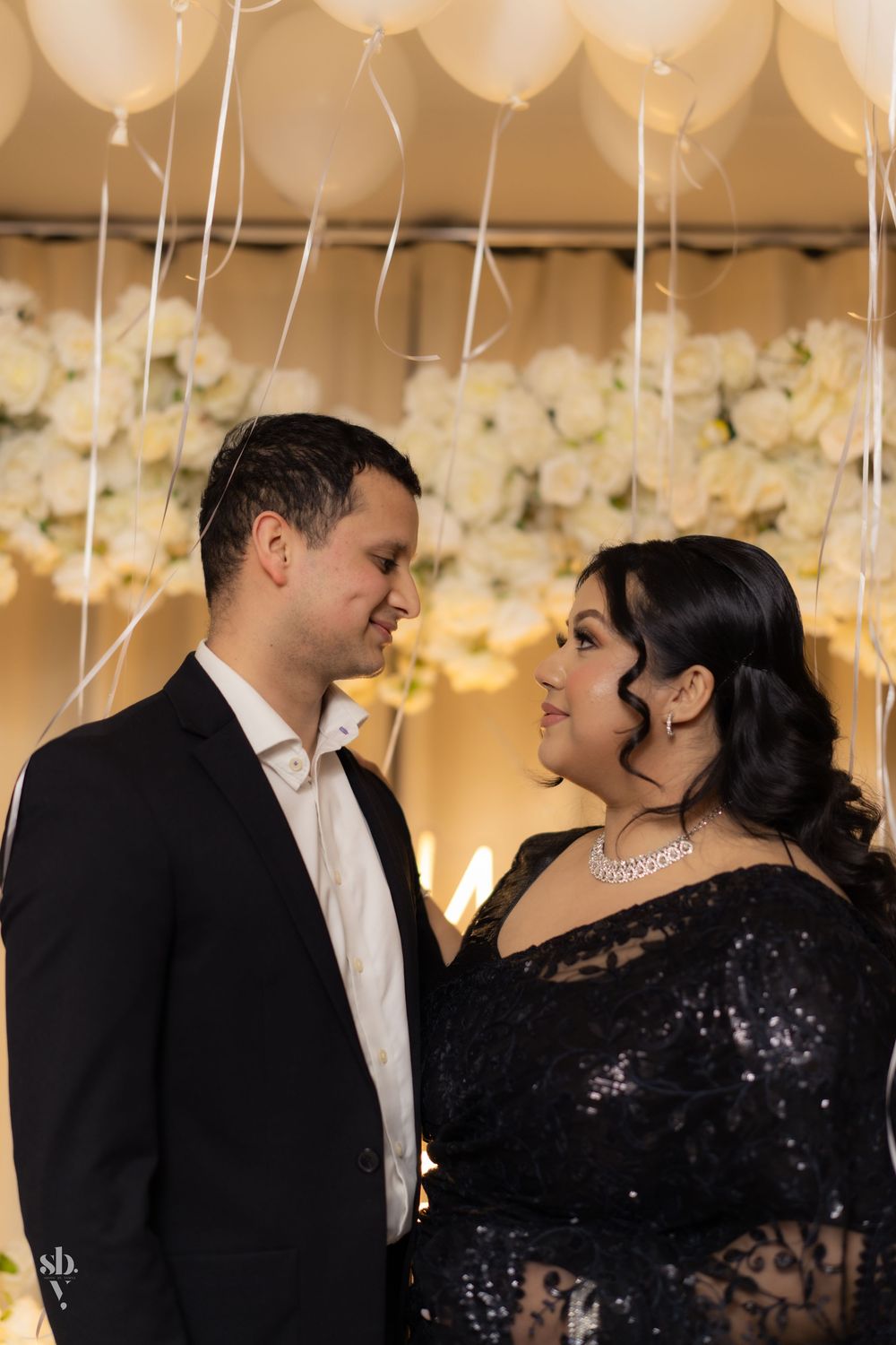 Couple shares intimate moment under white balloons and floral decorations at formal evening event.