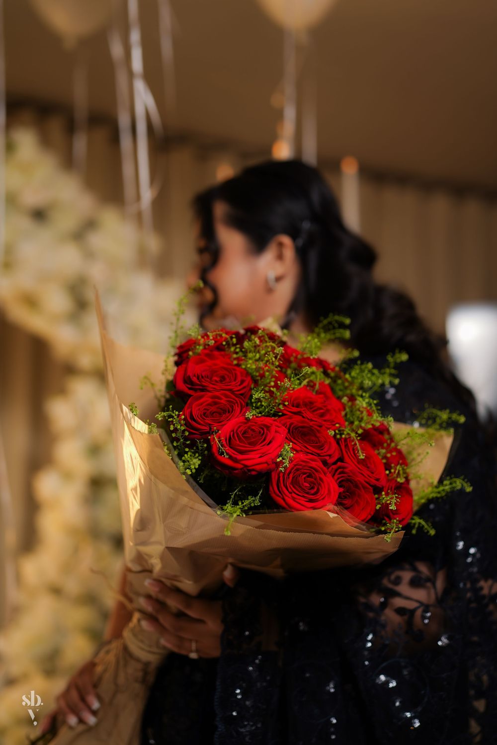A stunning bouquet of red roses and green foliage wrapped in brown paper is displayed in a warm-lit setting.