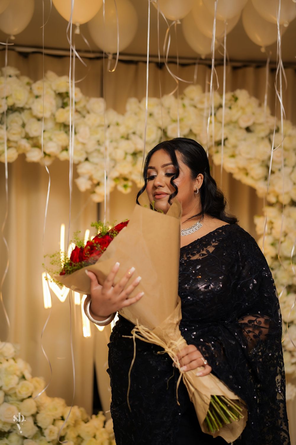 Four sequential celebration photos show an embrace with flowers and hanging light decorations against a floral backdrop.