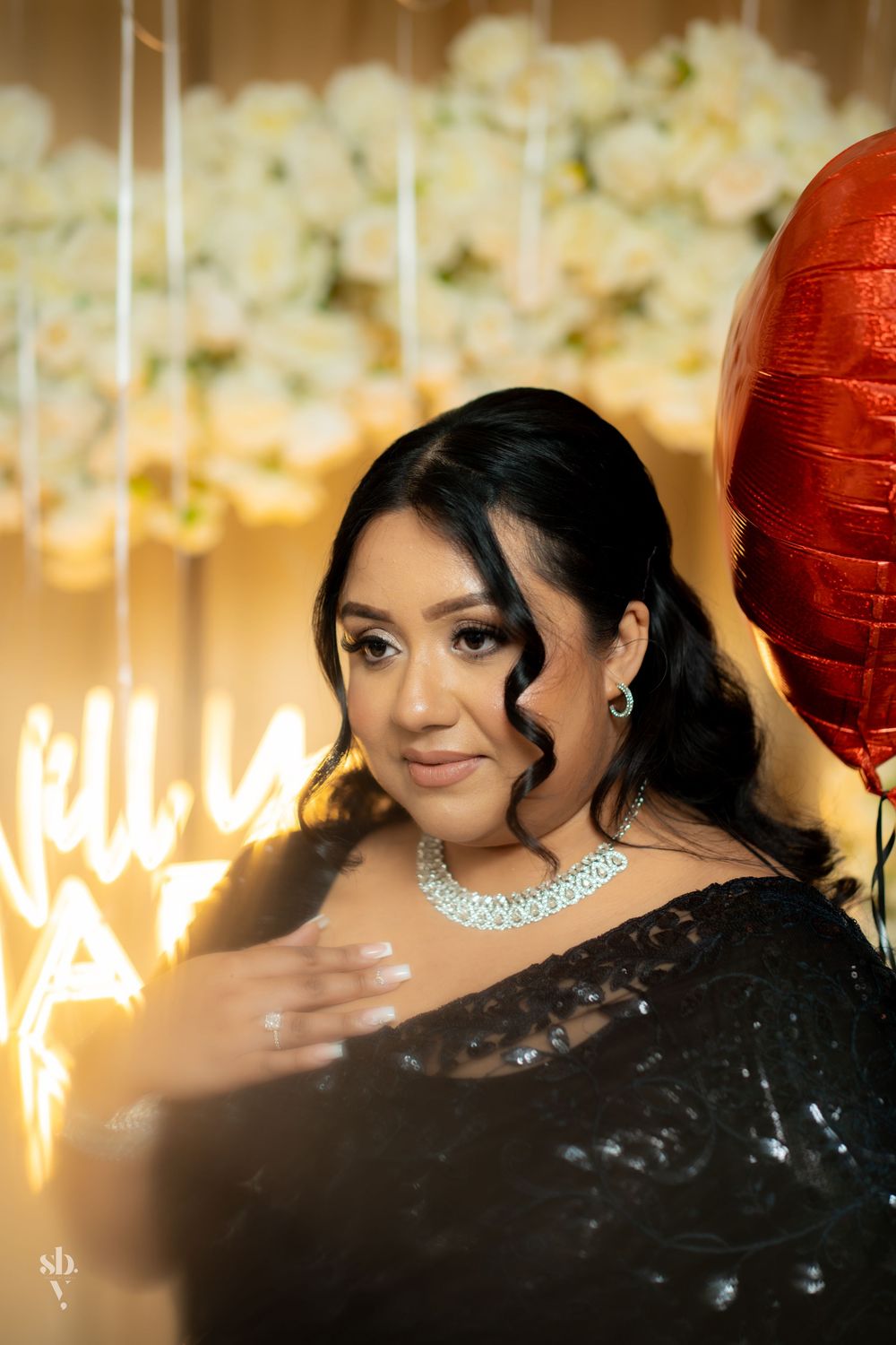 A glamorous celebration scene with sparkling decorative lights and red balloons in the background.