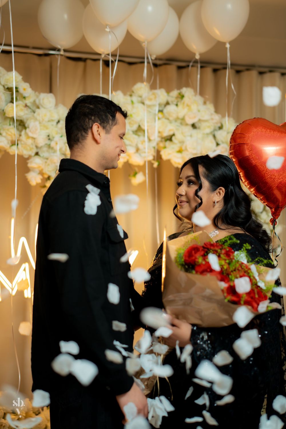 A romantic moment with confetti falling and decorative balloons in the background at an indoor celebration.