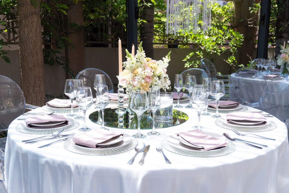 Elegant round table setting with white linens, floral centerpiece and wine glasses for formal dining.