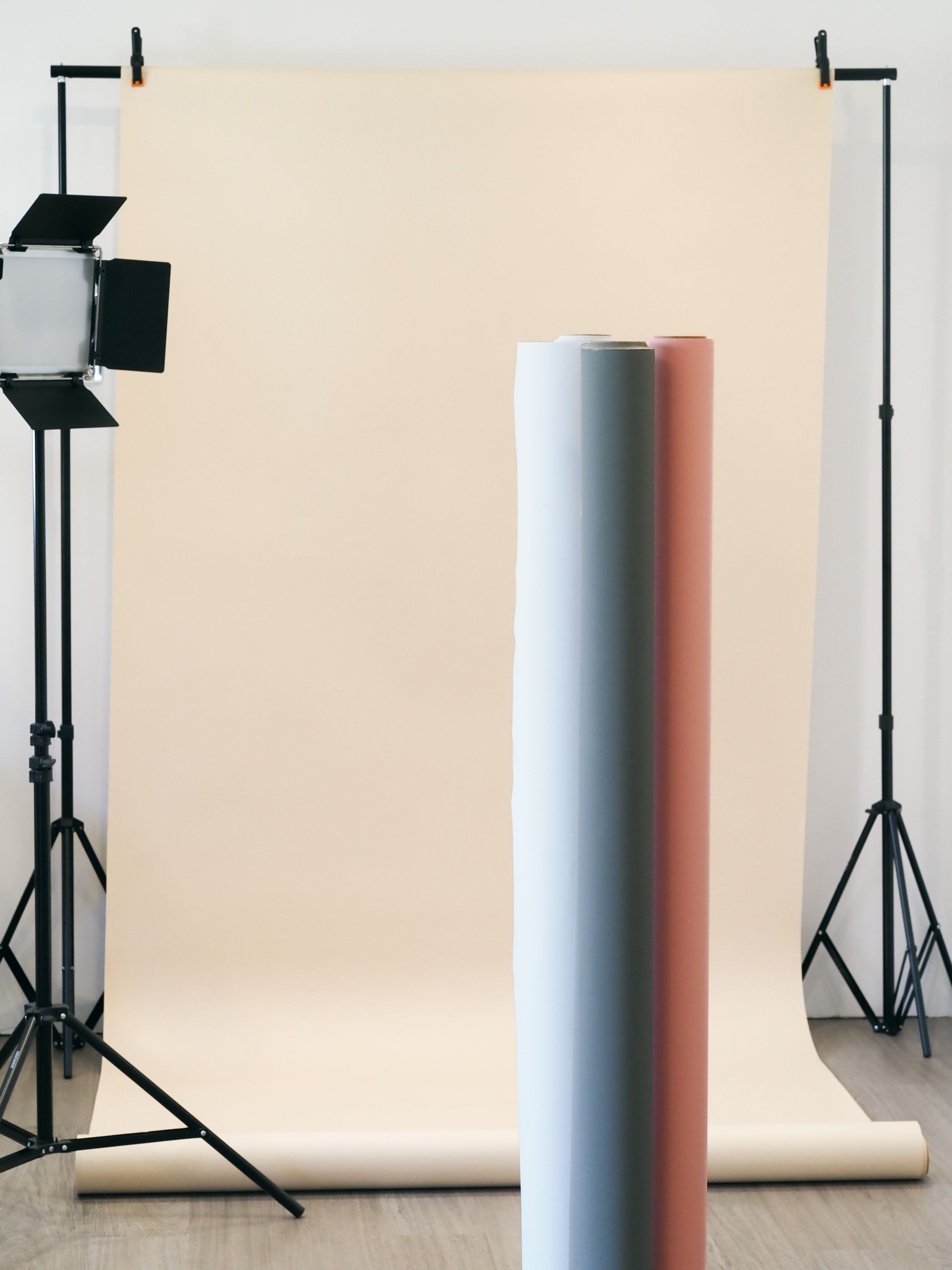 Photography studio setup with light stand and seamless white backdrop roll against beige wall.