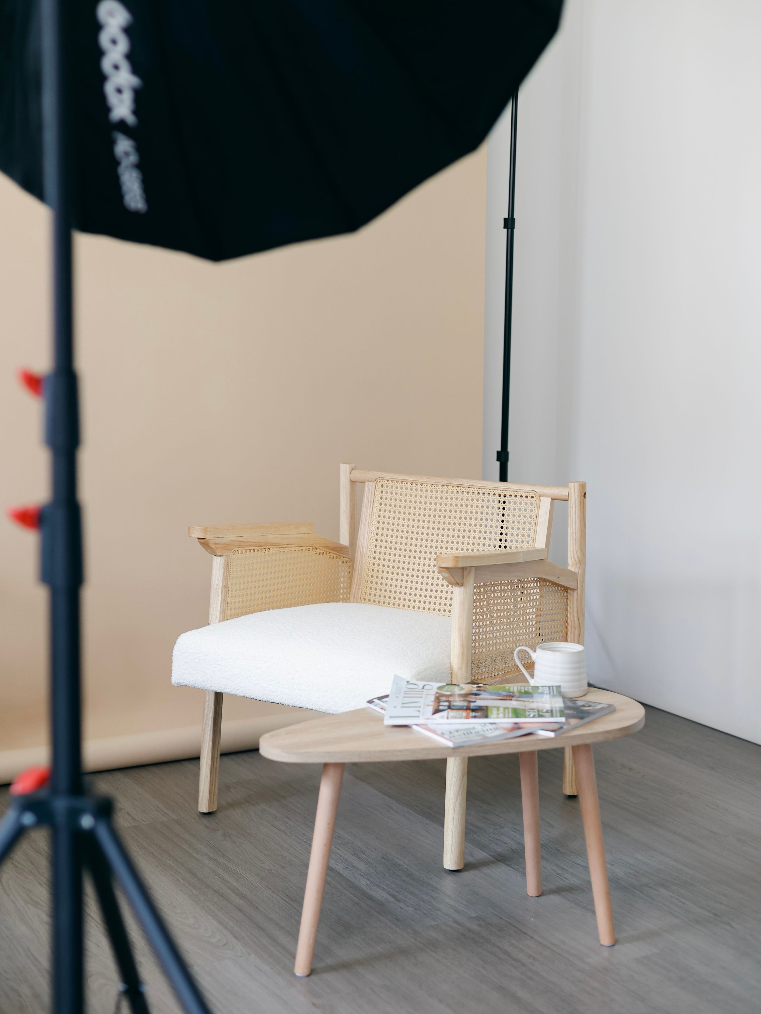 Modern wooden and cane chair with white cushion next to small round coffee table in photo studio setup.