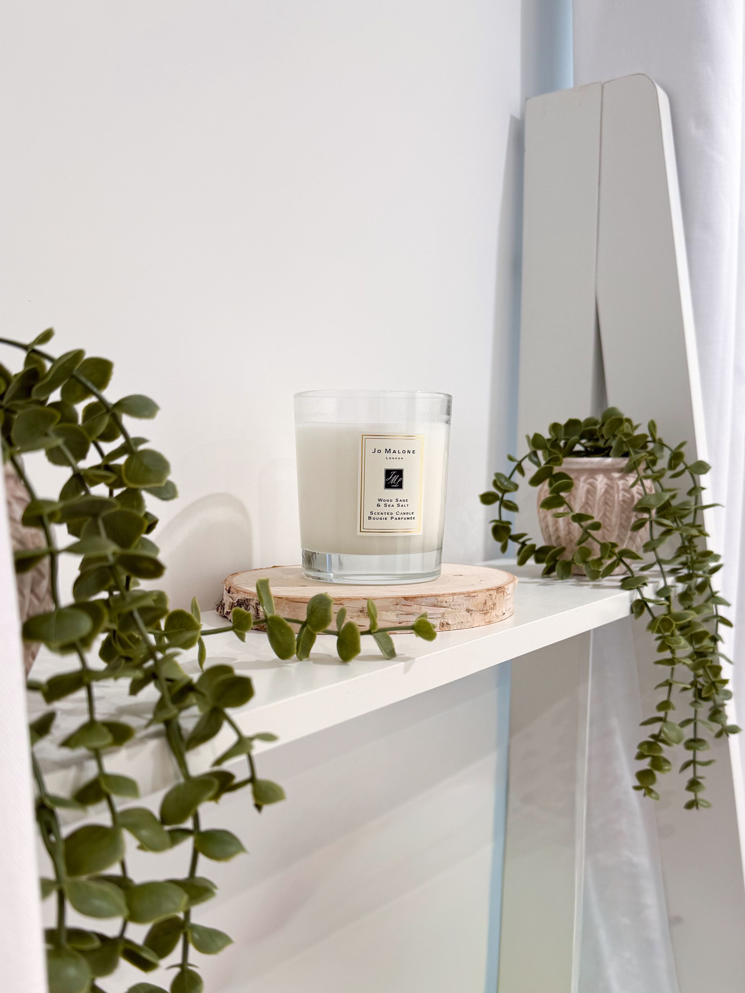 White floating shelves with cascading green plants and decorative objects create a minimalist wall display arrangement.