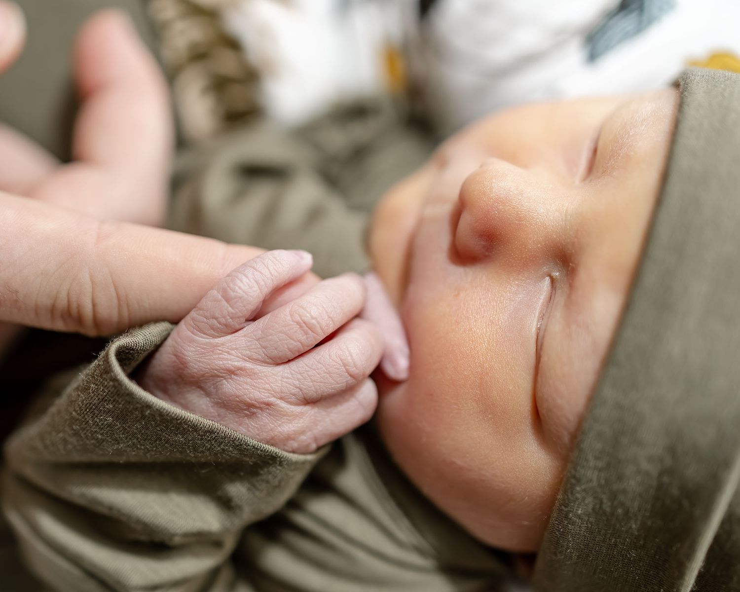 A tender moment captured as tiny fingers grasp an adult's hand in soft lighting.