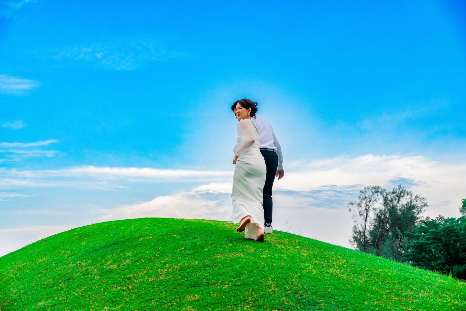 Figure stands on green hilltop against bright blue sky with flowing fabric in the wind.