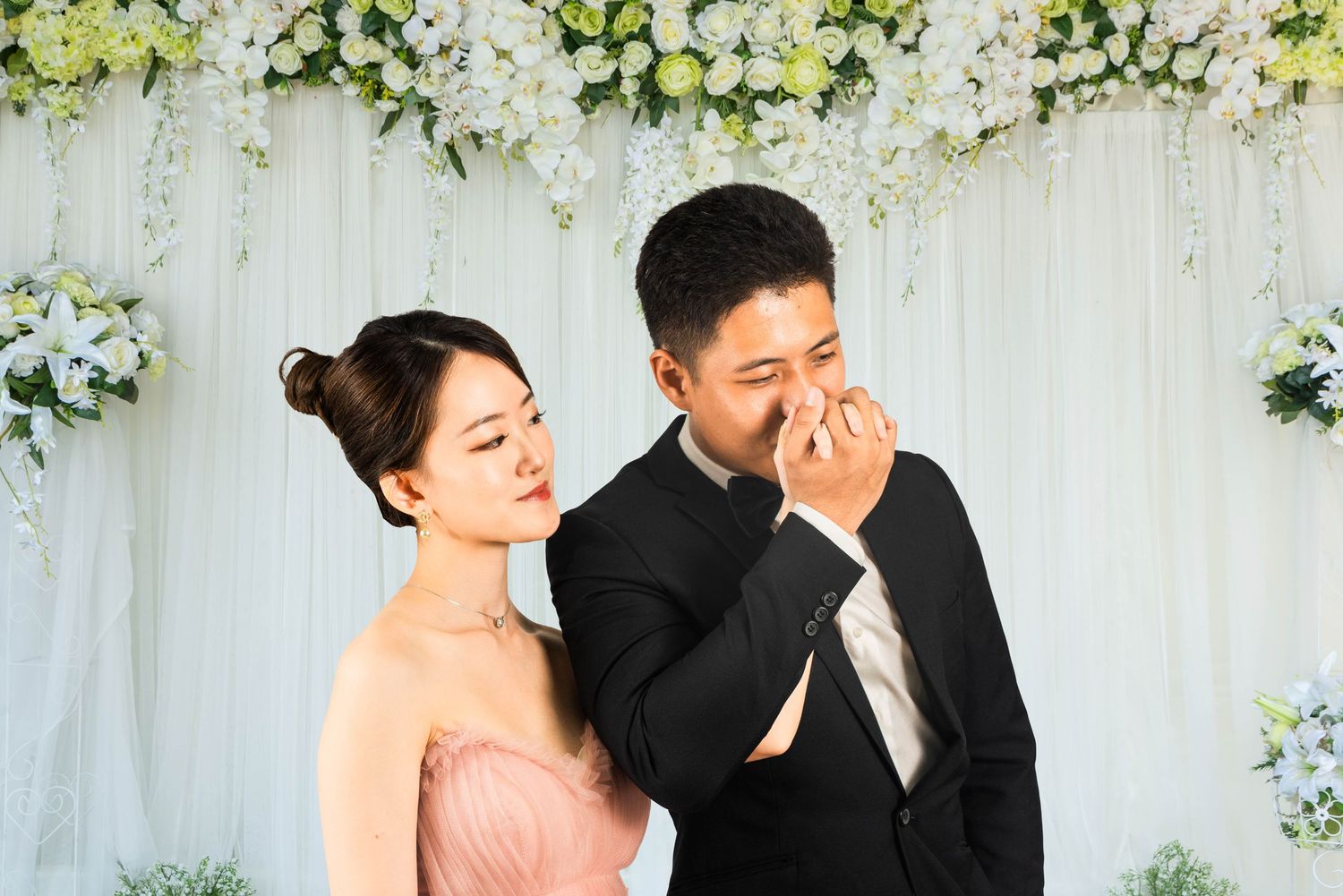 Couple shares tender moment against floral backdrop at wedding.