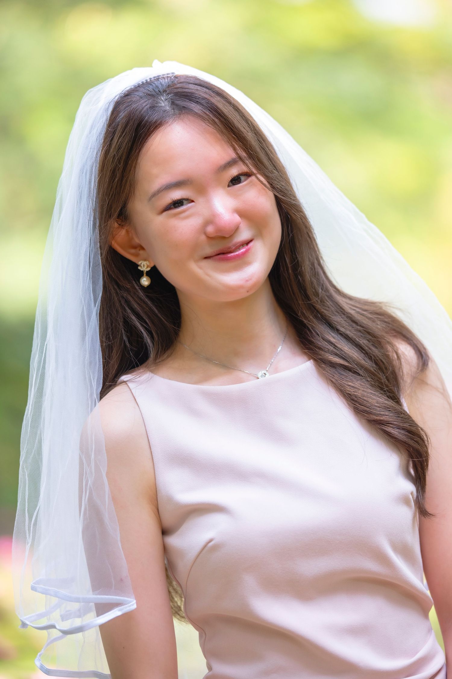 A bride in a white veil and sleeveless dress poses outdoors with a joyful expression.