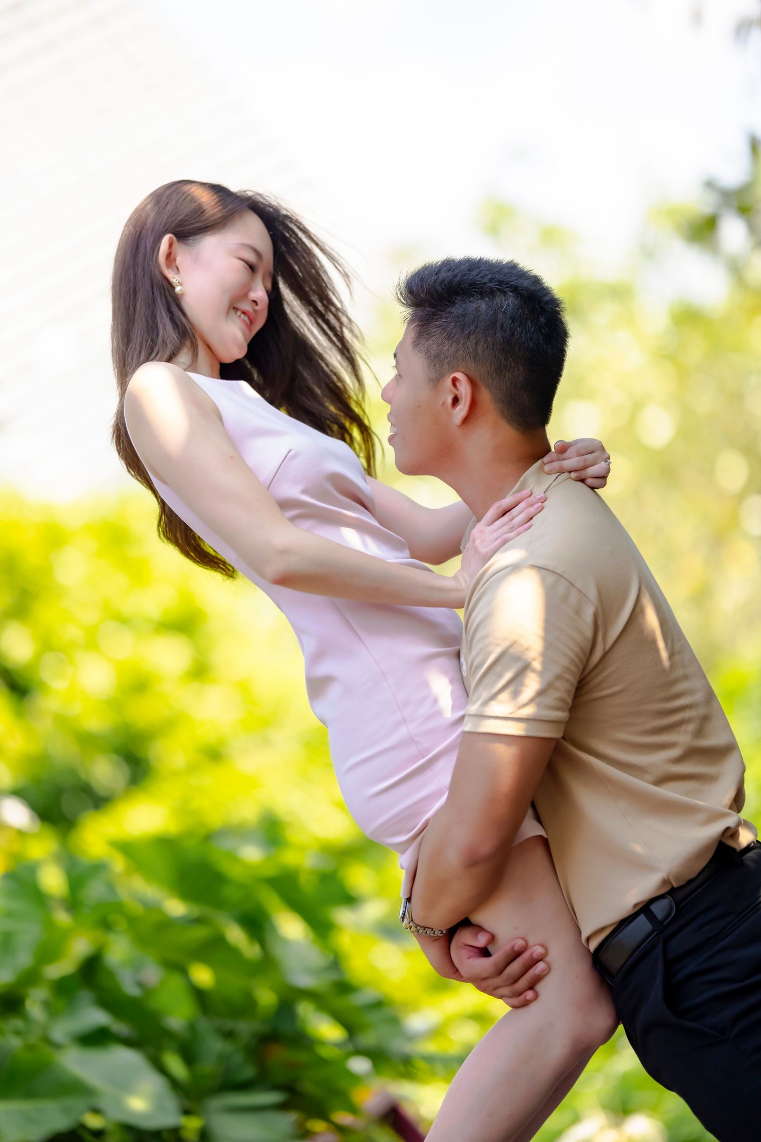 Couple in playful embrace outdoors with bright natural lighting.