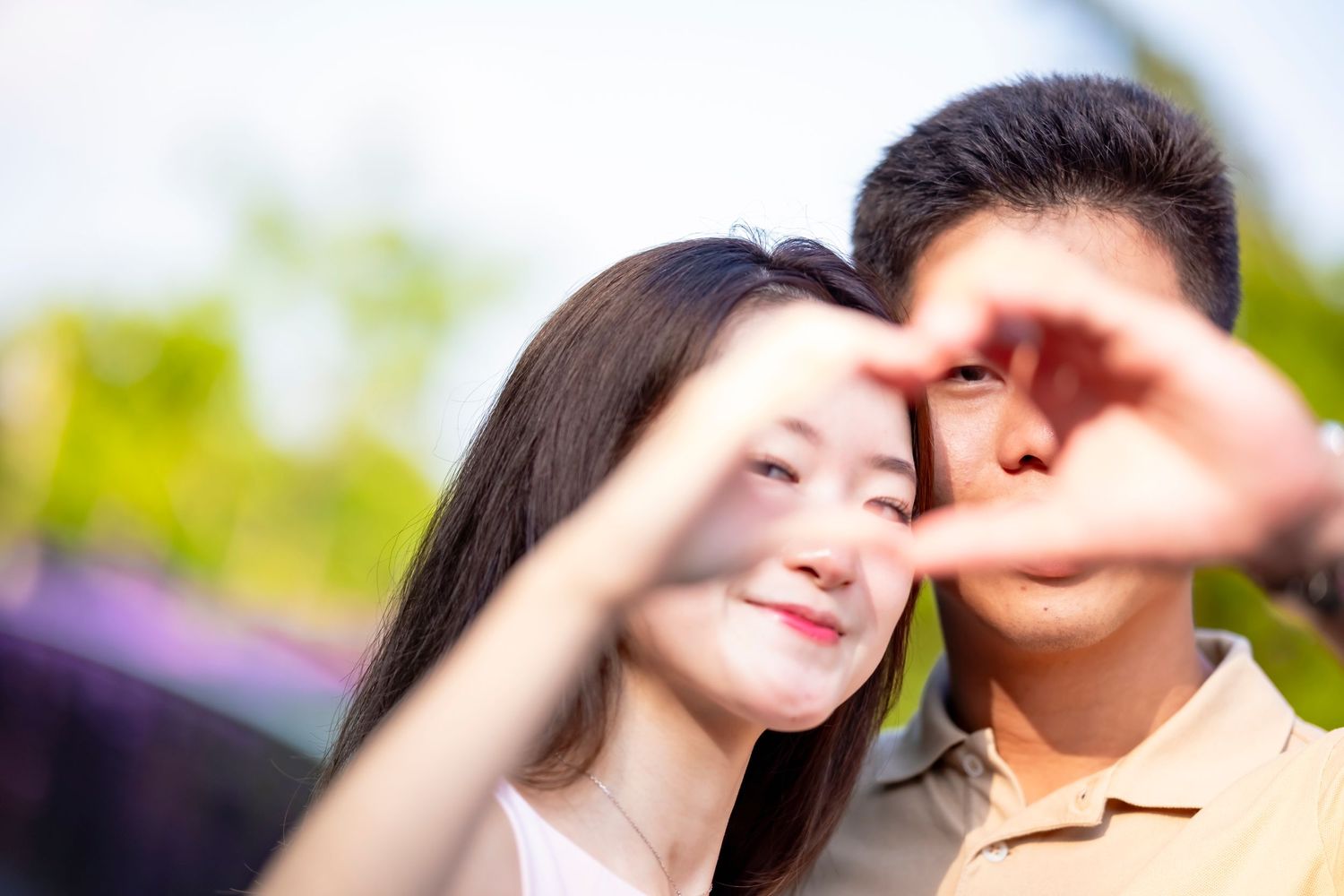 Romantic couple making heart shape with hands against blurred nature background.