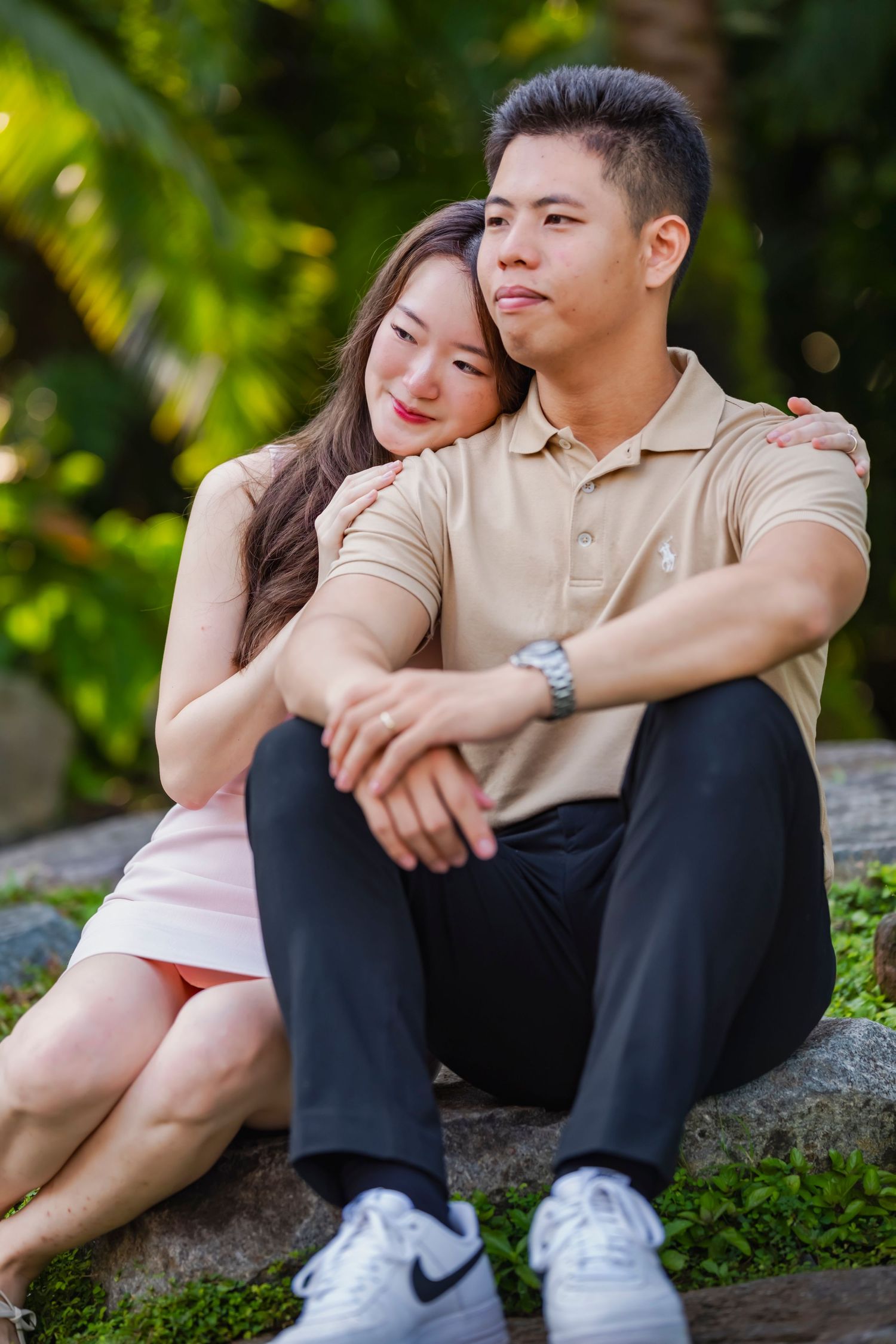 Couple relaxing on rock in garden wearing coordinated beige and pink outfits.