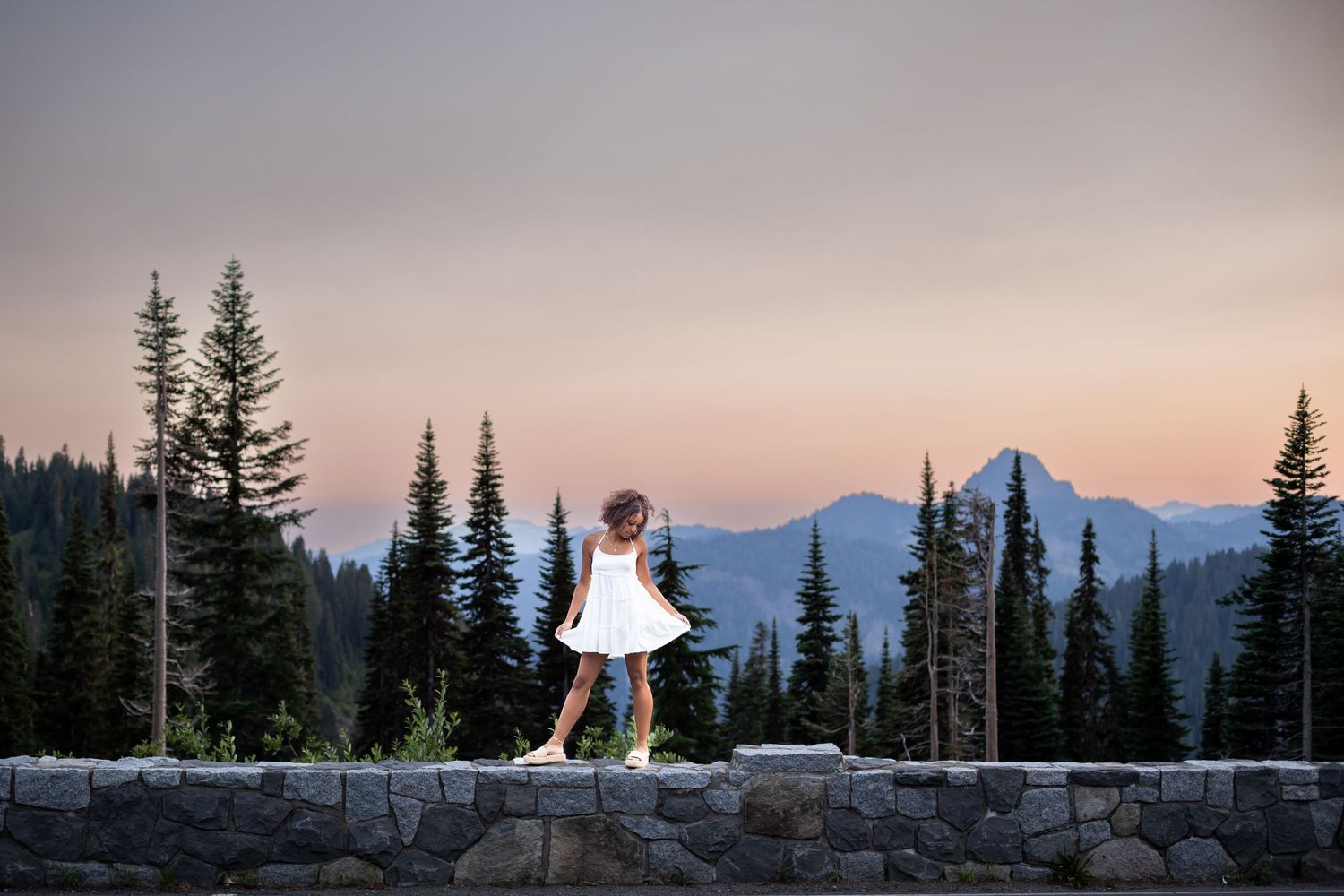 Silhouette of person in dress standing on wall with mountain vista at sunset.