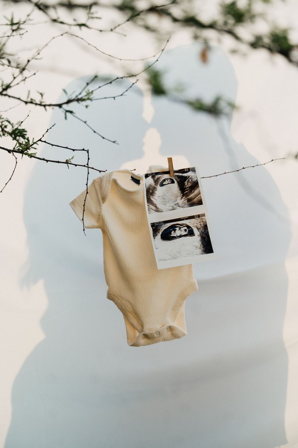 Baby onesie and ultrasound photos hung on a clothesline against a bright sky.