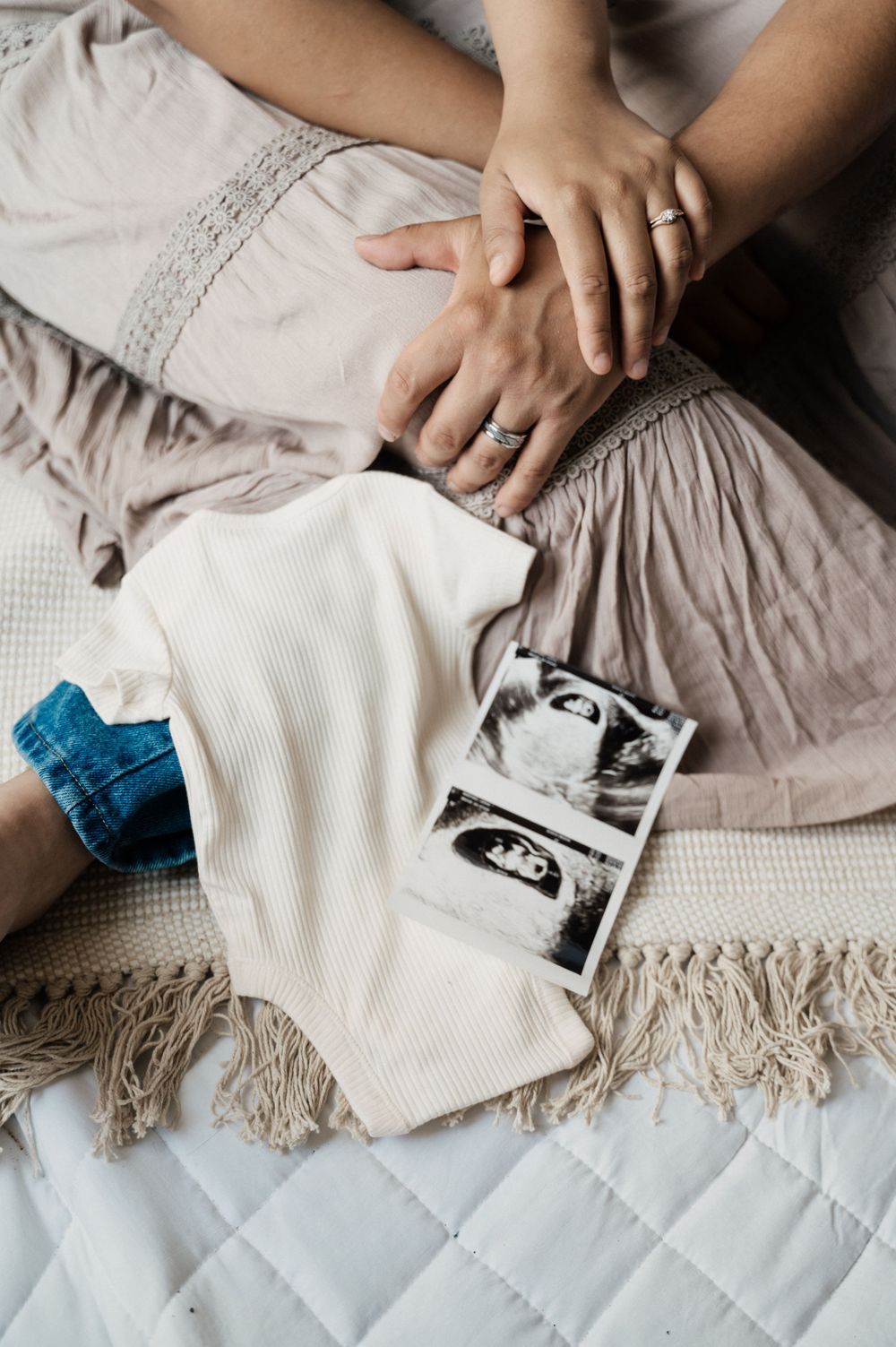 Hands rest on a quilted bed with ultrasound photos and a white blanket with a blue accent.