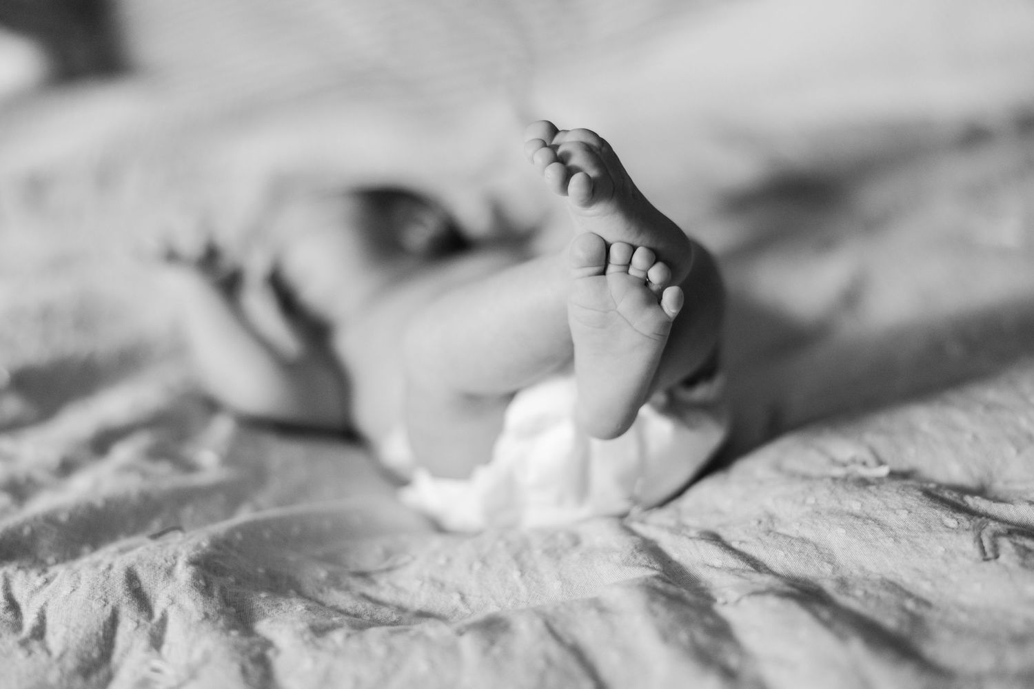 A black and white close-up photograph of tiny baby feet on wrinkled fabric.