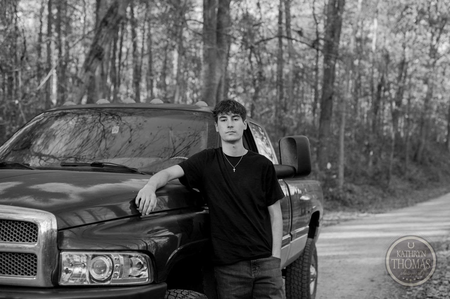 Black and white portrait with Dodge pickup truck parked on wooded dirt road.