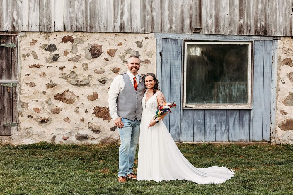 Rustic outdoor wedding portrait in front of a stone wall with weathered blue window.