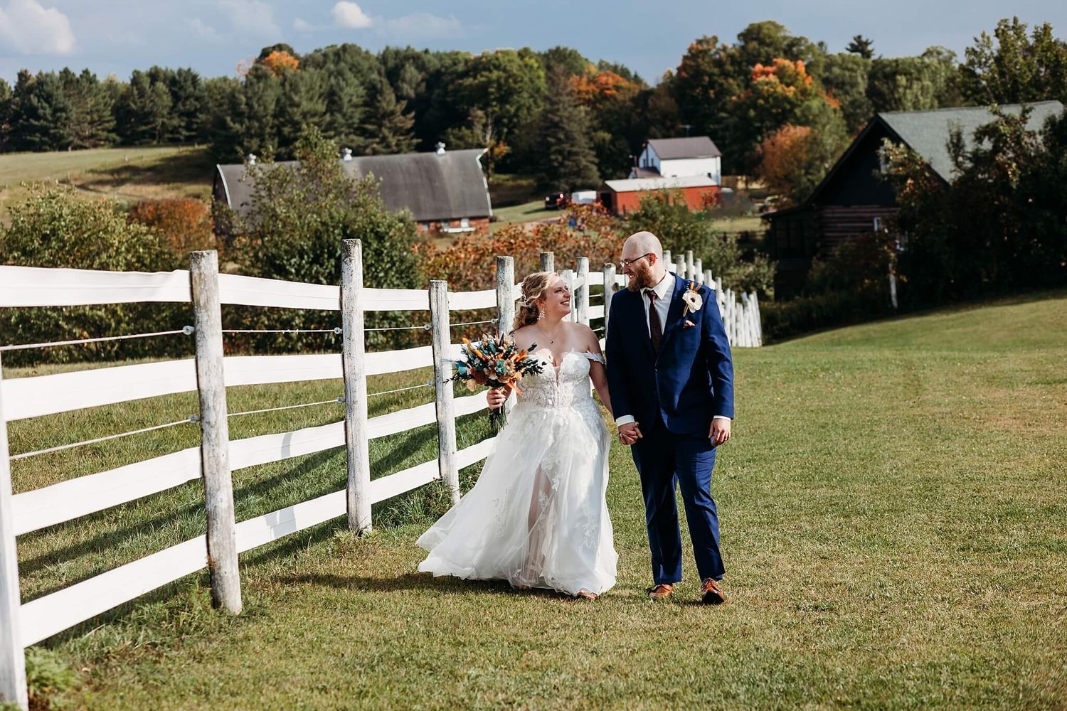 bride and groom walking along white picket fence during couple portraits at their outdoor wedding