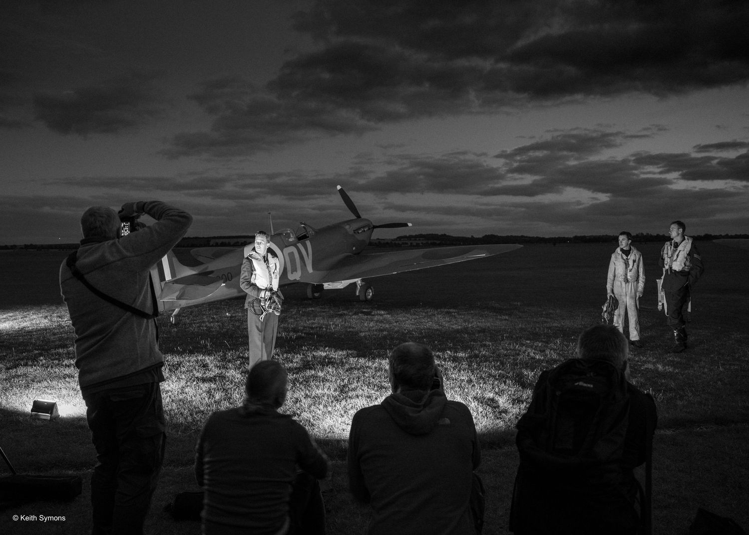 A nighttime black and white photo shoot scene with crew and lighting equipment.