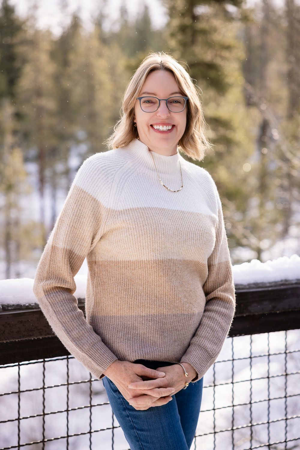 A woman poses outside with trees and snow in the background