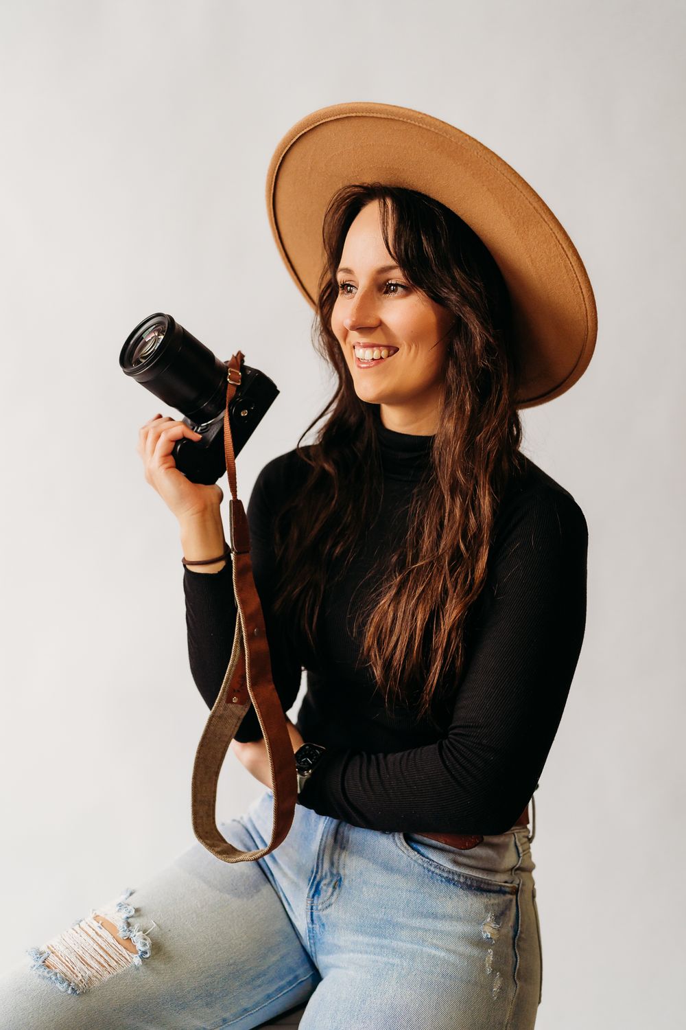Photographer in black turtleneck and brown hat holding vintage camera.
