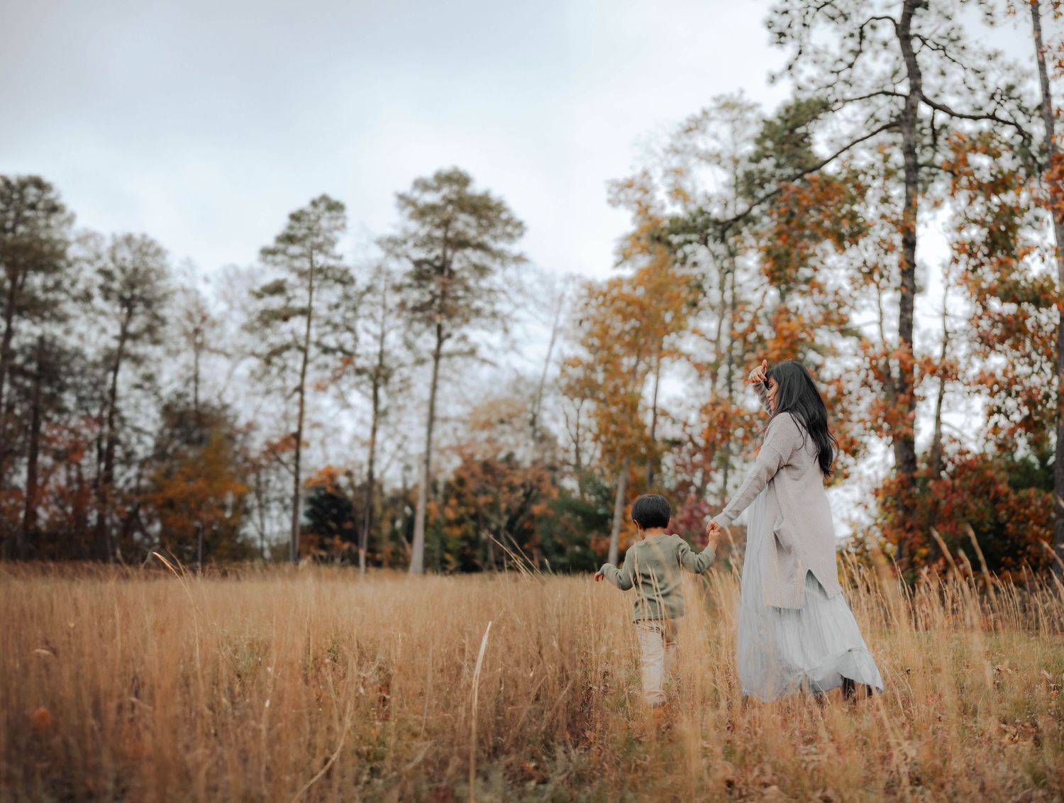 Couple in white outfits playing in a golden autumn field with tall pine trees.