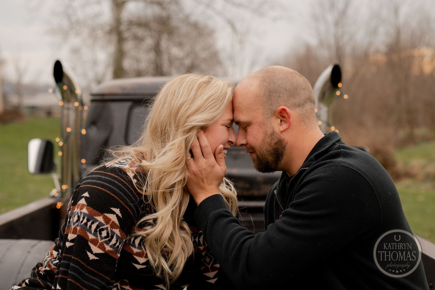 A couple shares an intimate moment in front of a classic truck during an outdoor photo session.