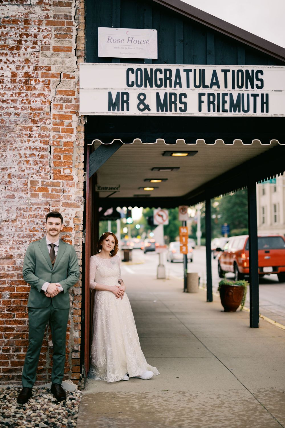 Wedding couple poses by brick wall under sign reading 'Congratulations Mr & Mrs Friemuth' in downtown storefront.