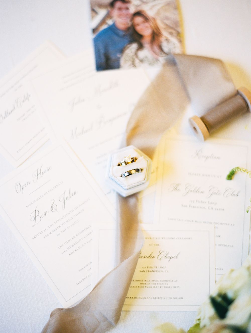 Wedding invitation suite with rings, stationery and engagement photo on light background.