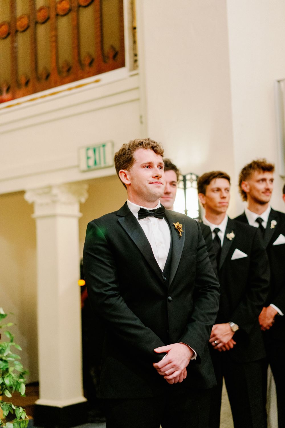 Groomsmen in black tuxedos stand awaiting the ceremony in an elegant church setting. Presidio Chapel wedding ceremony photos.