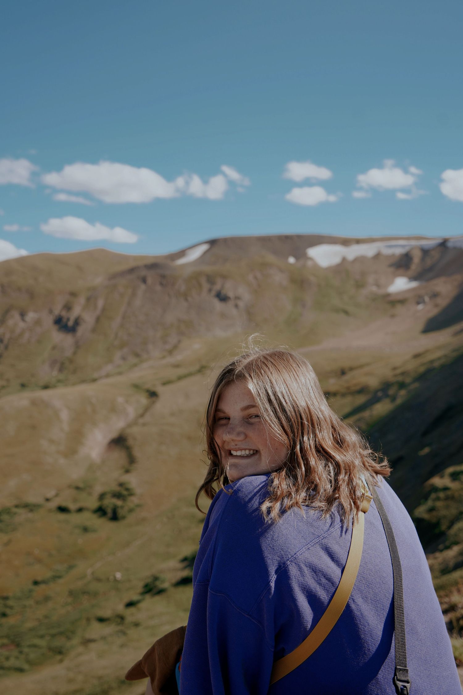 Smiling young woman in blue jacket looking back on mountain summit under blue sky.