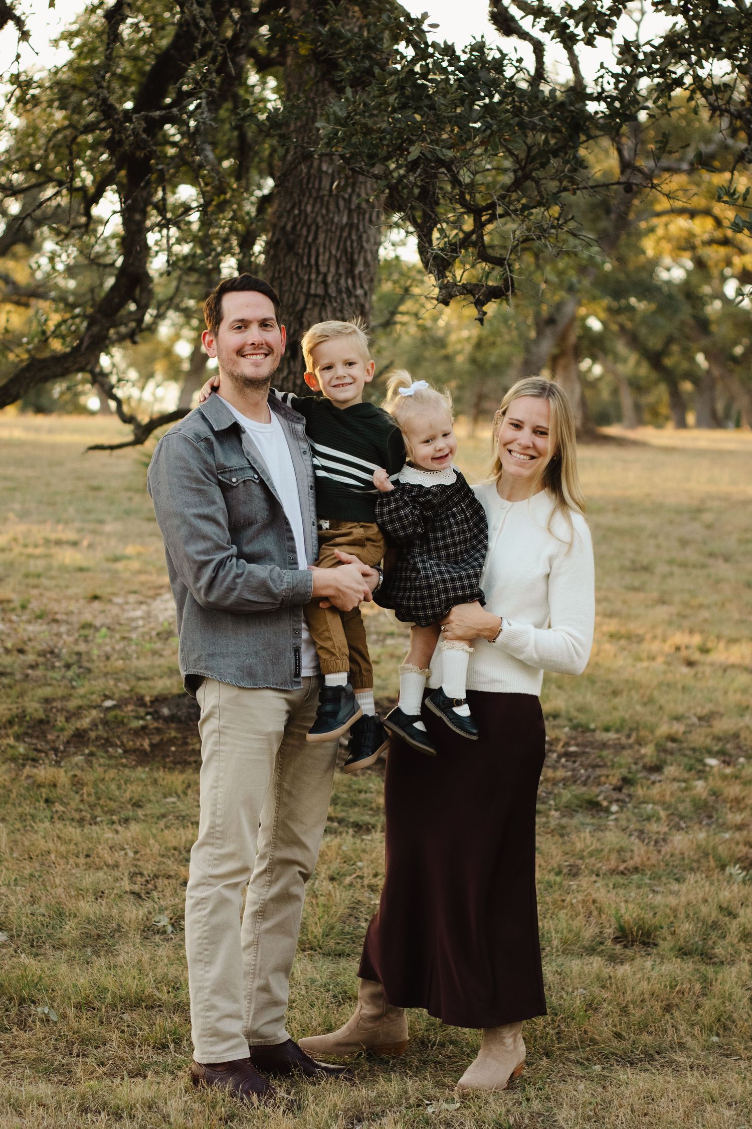 Family portrait in casual attire against backdrop of autumn trees at sunset.