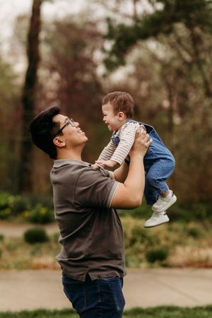 Father lifting laughing baby boy up in the air at outdoor park.