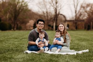 Young family with twin babies sitting together on blanket in green park.
