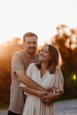 A smiling couple embraces warmly outdoors during a beautiful golden hour sunset in nature.