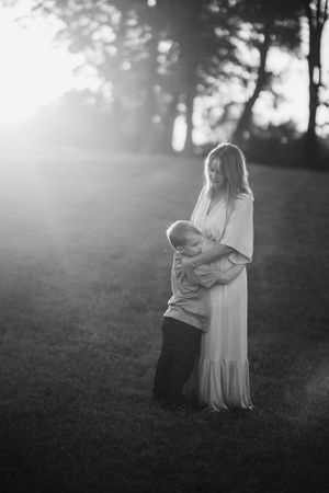 A black and white photo of a mother and son sharing a tender embrace in a sunlit grassy field.